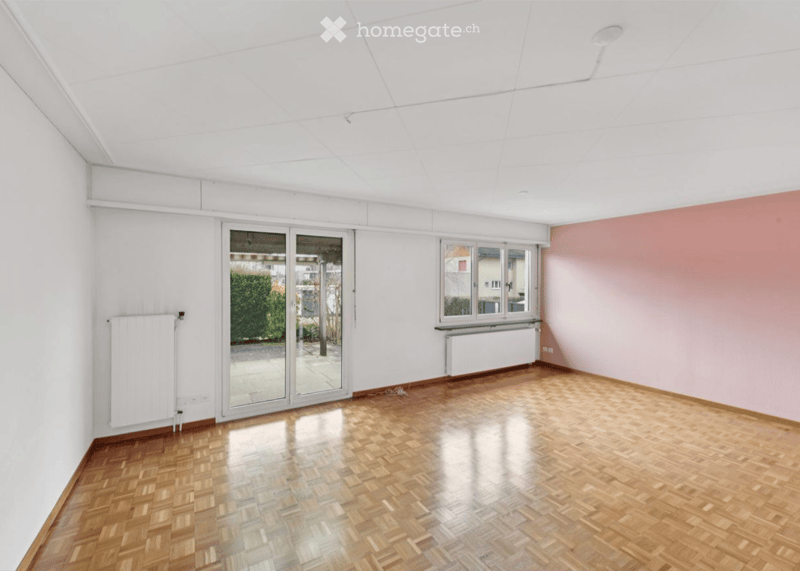 Empty room with wooden flooring, white walls, large sliding glass doors, and a window with radiator below.
