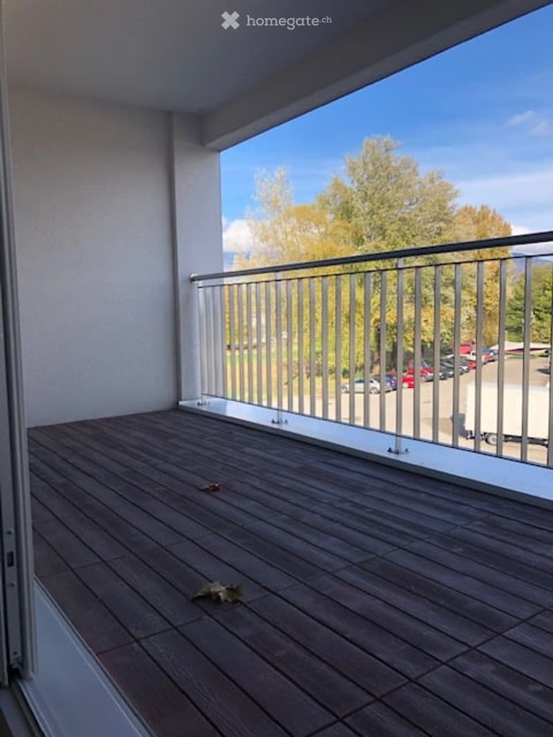 wooden balcony, metal railing, large windows, view of trees and parking lot