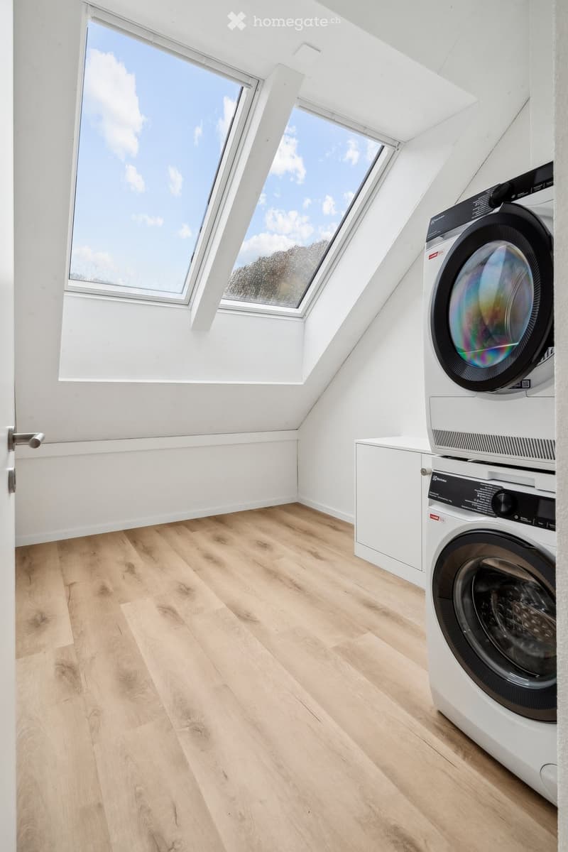 wooden floor, white walls, stacked washer and dryer, attic window