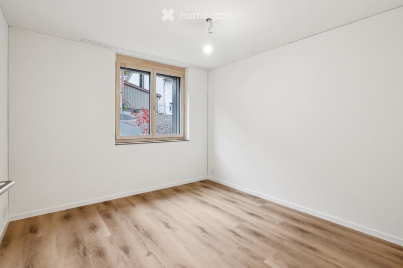 Empty room with white walls, wooden flooring, and a large window with a view of the outside.