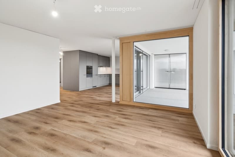 Empty room with wooden floor, white walls, large windows, and a view of another room.