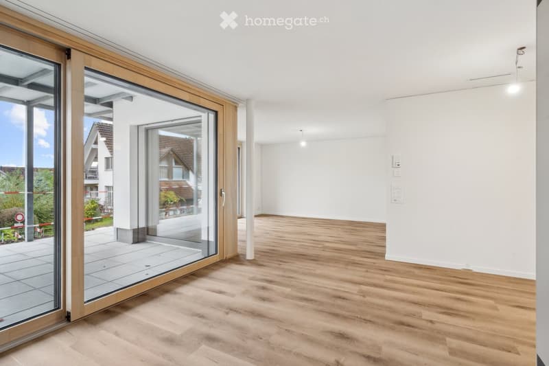 Empty room with light wooden flooring, white walls, and large glass sliding doors leading to a balcony or outdoor area.