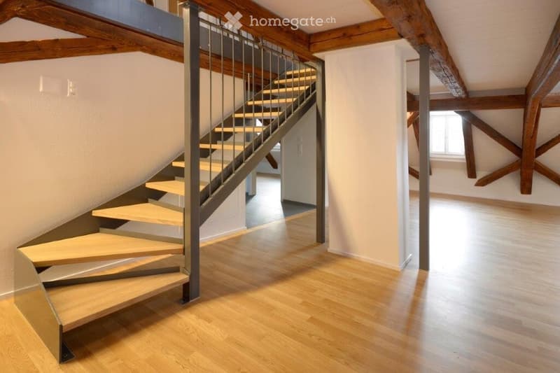 Modern hallway with wooden flooring, exposed wooden beams, and a staircase with metal railing leading to an upper level.