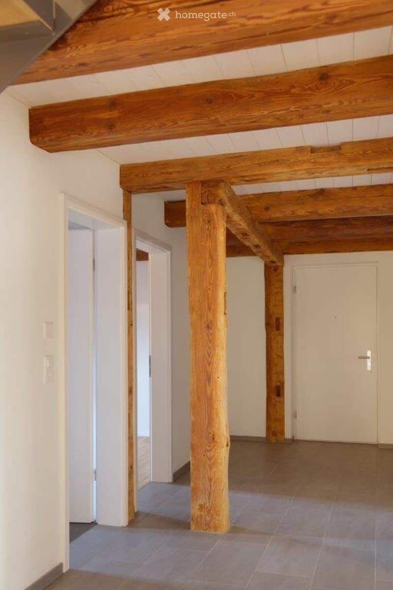 Empty hallway with exposed wooden beams and columns, tiled floor, white walls, and several doors.