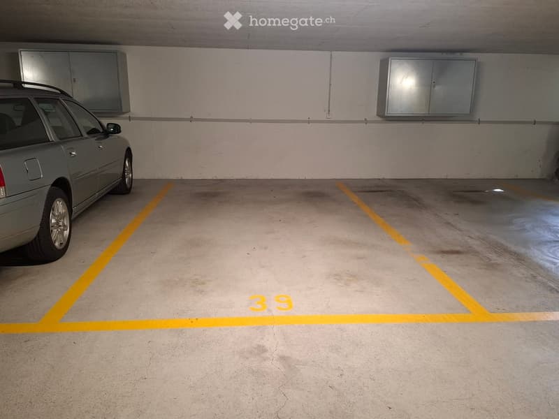 Underground parking space with a marked parking spot number 39, a parked car, and metal cabinets on the walls.