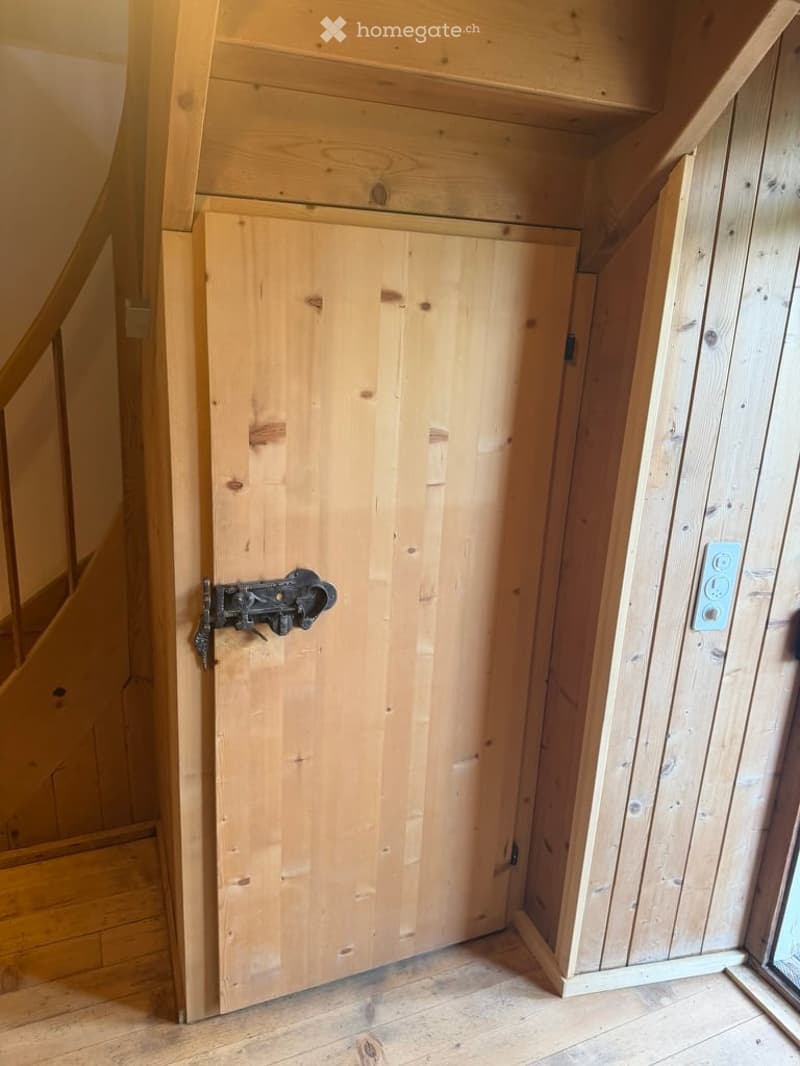 Empty wooden room with a closed wooden door, visible wooden floor, and a visible electrical outlet on the wall.