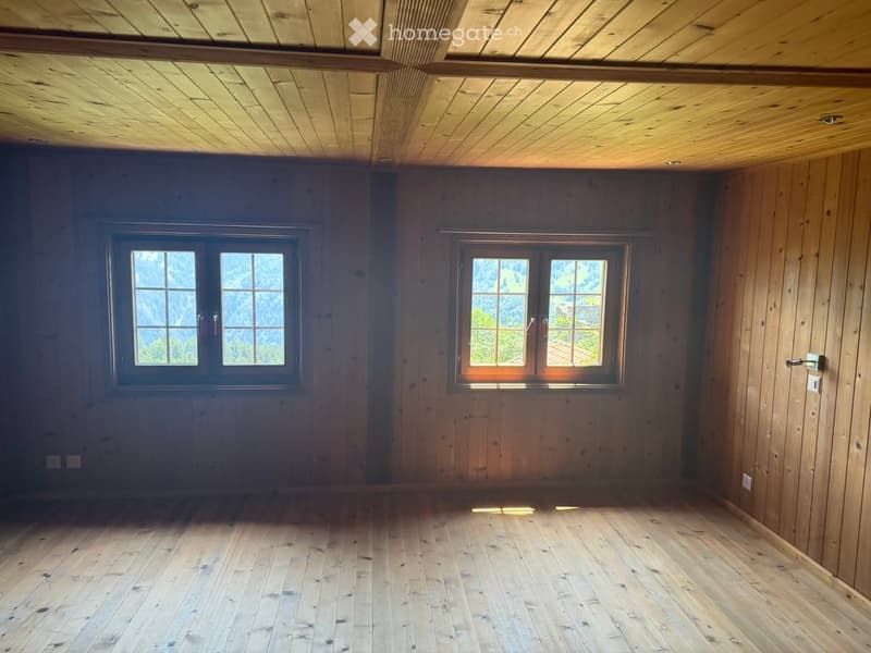 Empty room with wooden walls, ceiling, and floor, two windows with natural light, and no furniture.