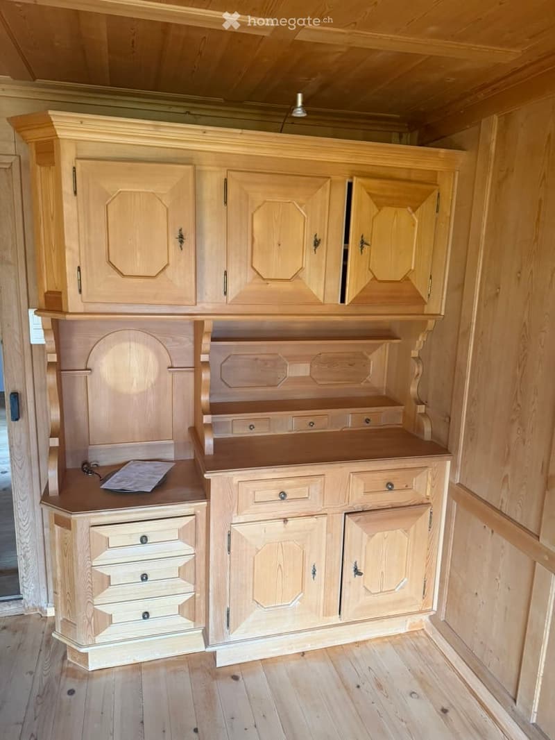 A well-furnished room with light wooden cabinets, a wooden desk, and multiple drawers, all set against a wooden-paneled wall and floor.