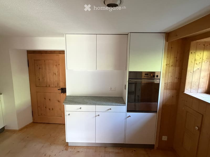 Modern kitchen with white cabinets, a stainless steel oven, and a granite countertop. Wooden flooring and a wooden door are visible.