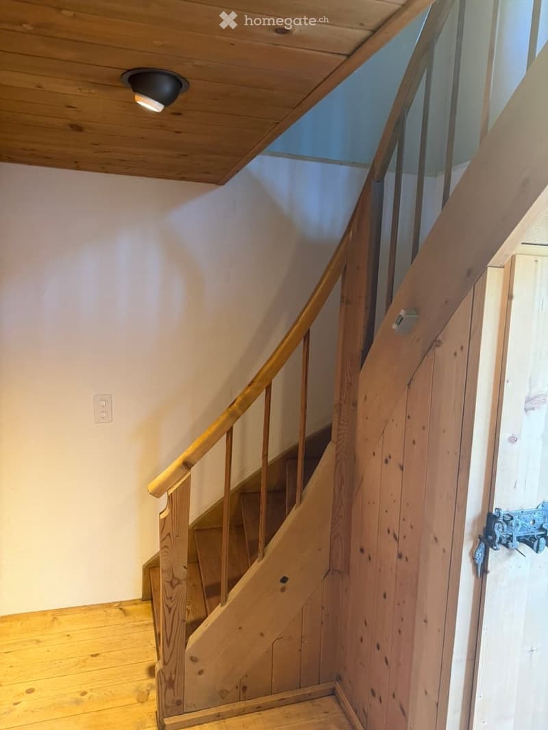 Wooden staircase with a handrail, wooden floor, and a wooden door with a metal handle.