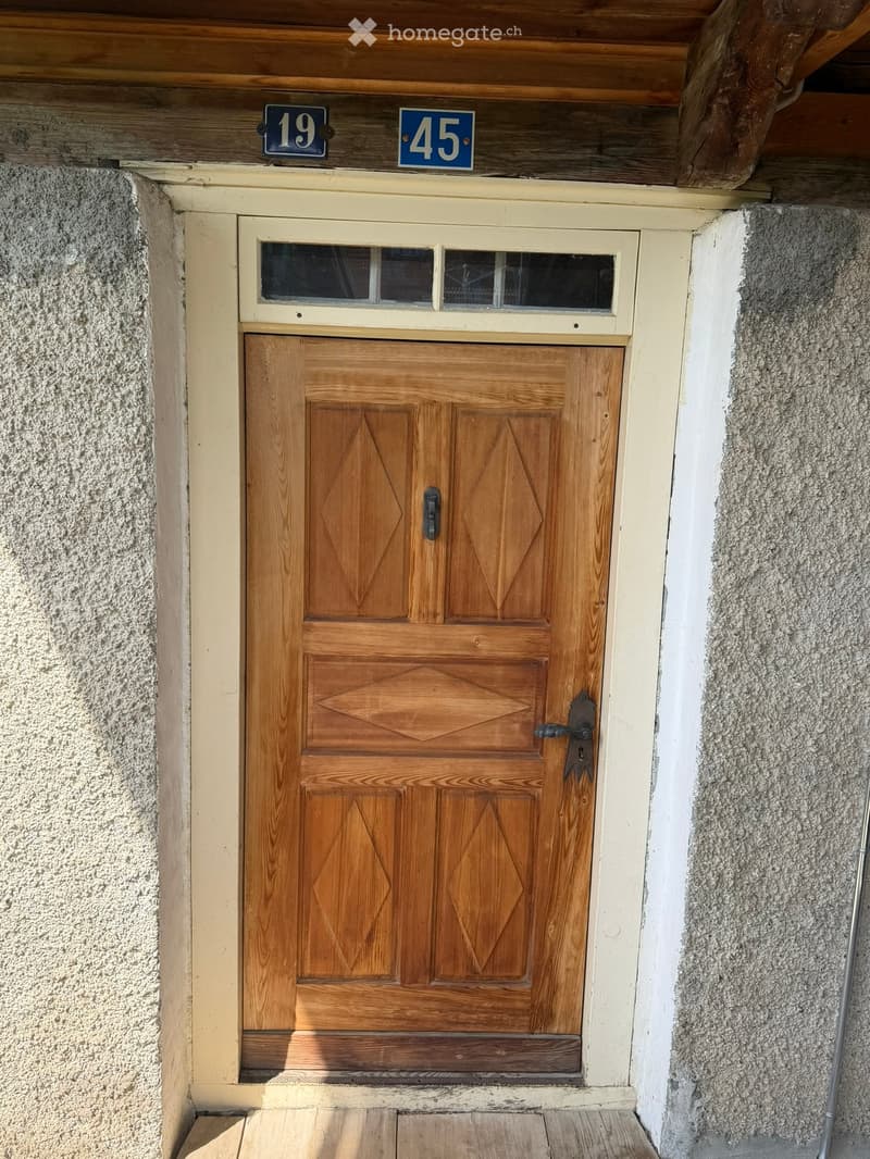 Wooden double door with decorative diamond patterns, small window above, and house numbers 19 and 45 displayed above the door.