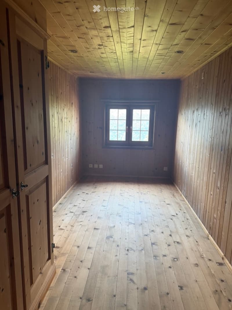 Completely empty room with wooden walls, ceiling, and floor. A single window is visible on one wall, and a door is on the left side.