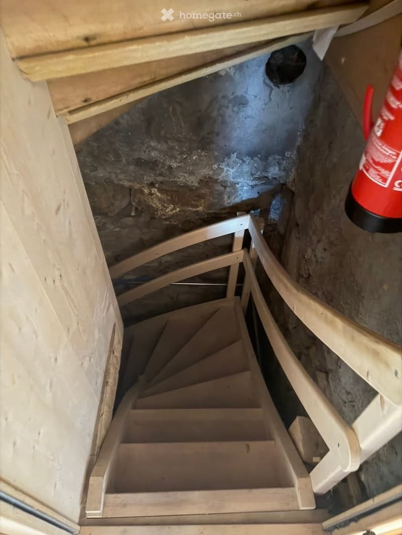 Wooden staircase leading to a basement area with exposed stone walls and unfinished construction materials visible.