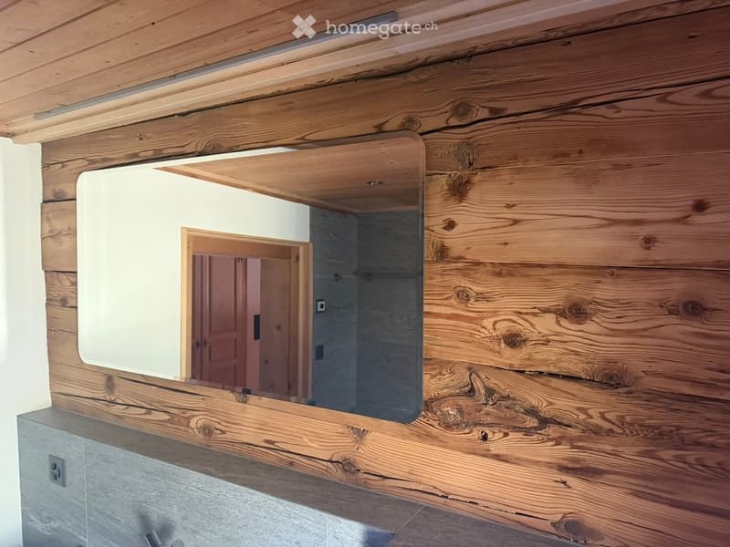 Bathroom with wooden wall paneling and a large rectangular mirror mounted on the wall.