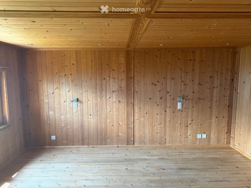 Empty room with wooden walls and ceiling, wooden floor, and a small window on one side.