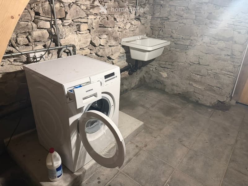 Bathroom with stone walls, tiled floor, white washing machine, and a small sink.
