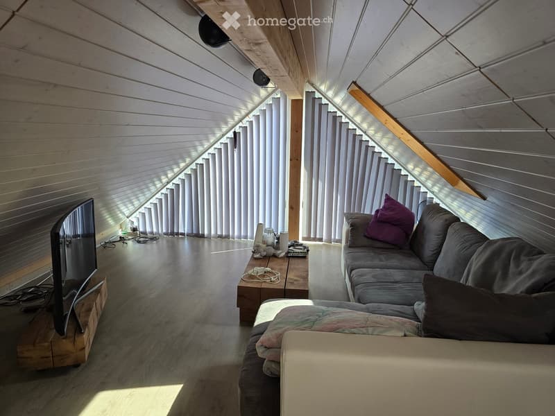 Living room with wooden slatted ceiling, large windows with blinds, sofa, coffee table, and television on a wooden stand.