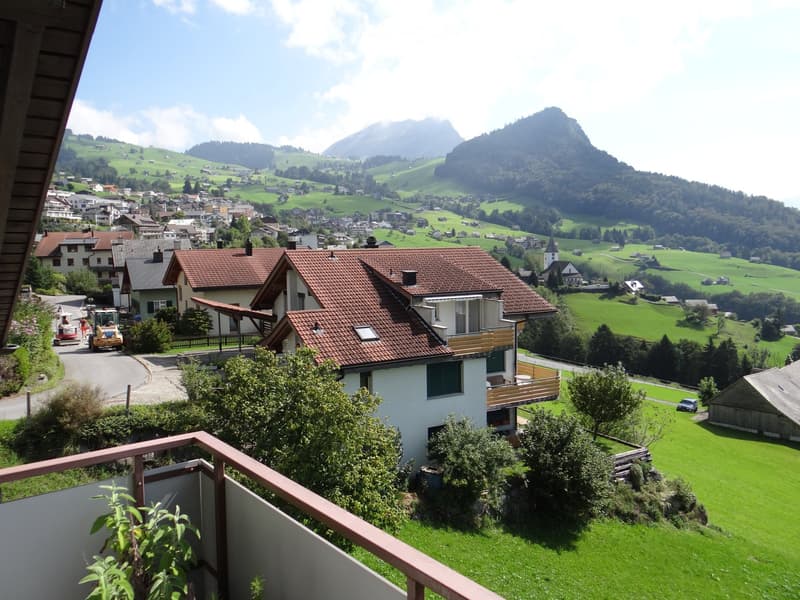 Balcony overlooking a picturesque village with green hills, houses, and distant mountains.