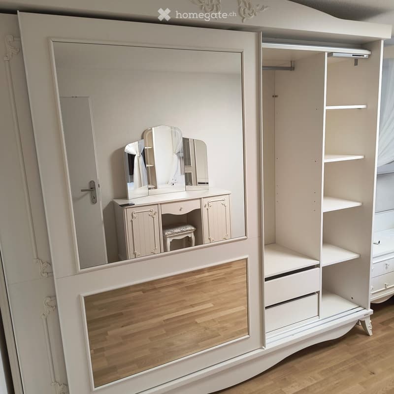 Elegant bedroom with a large mirrored wardrobe, a vanity dresser with a stool, and a small mirror on top.