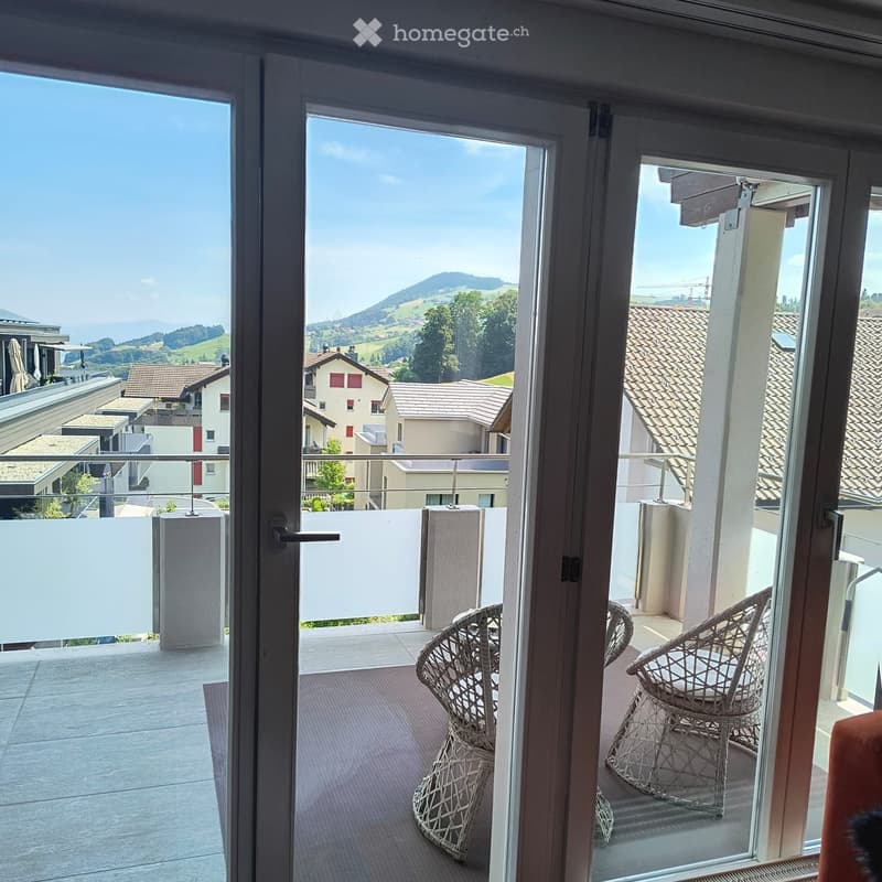Balcony with two wicker chairs, overlooking a scenic landscape with hills and houses.