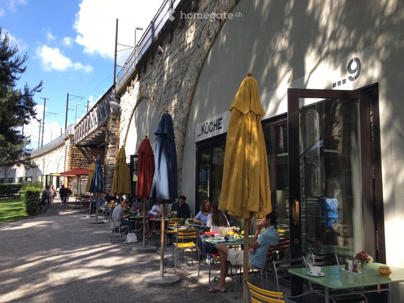 Outdoor seating area of a restaurant with tables, chairs, and umbrellas, people sitting and enjoying the space.