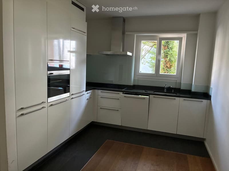 Modern kitchen with white cabinets, stainless steel appliances, black countertops, and a window overlooking greenery.