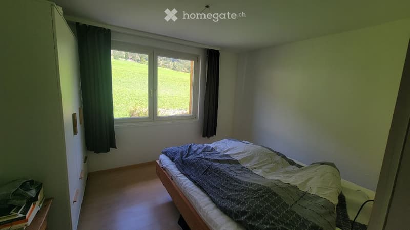 Bedroom with a wooden bed, a wardrobe, and a window with a view of a green field.