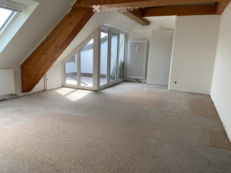 Empty attic room with exposed wooden beams, large skylight, and sliding glass doors leading to a balcony.