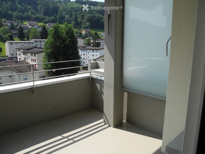 Balcony with metal railing, overlooking a residential area with houses and trees.