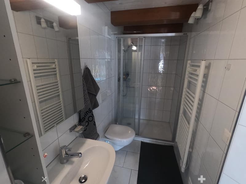 Modern bathroom with white tiles, a sink, toilet, shower, and a towel hanging on the wall.