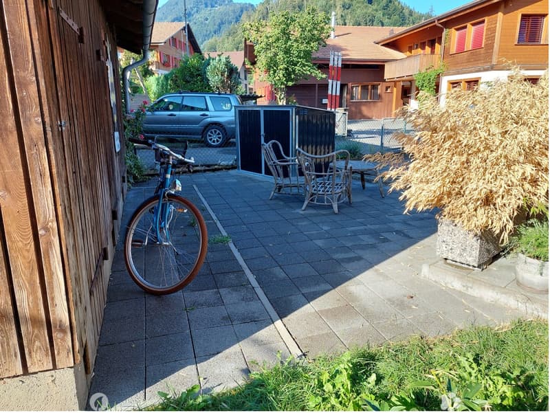 Outdoor patio area with tiled flooring, metal chairs, small table, bicycle, and potted plants.