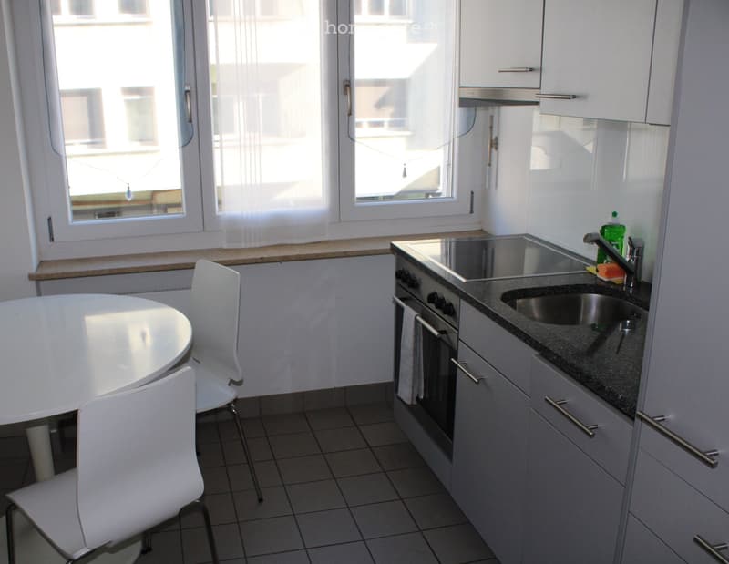 Modern kitchen with white cabinets, granite countertop, stainless steel sink, and a small dining area with a round table and two chairs.