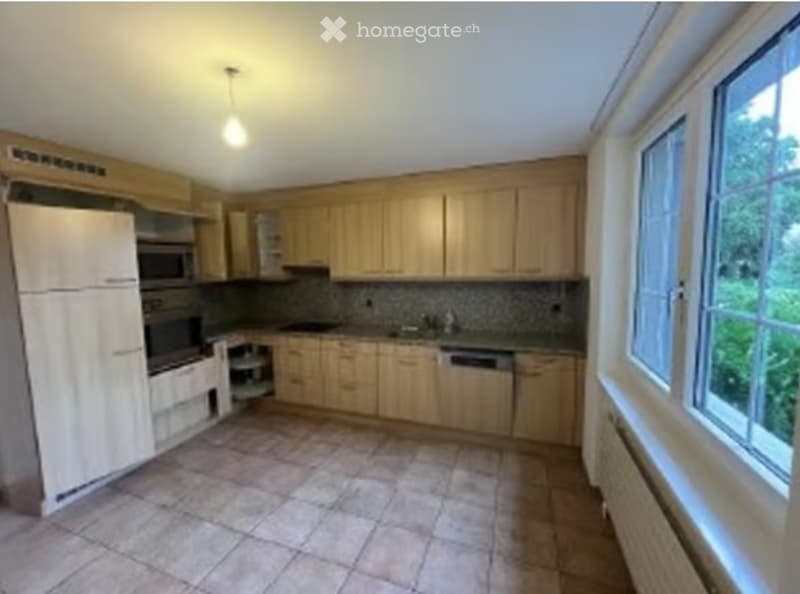 Bright kitchen with light wooden cabinets, stainless steel appliances, and tiled flooring.