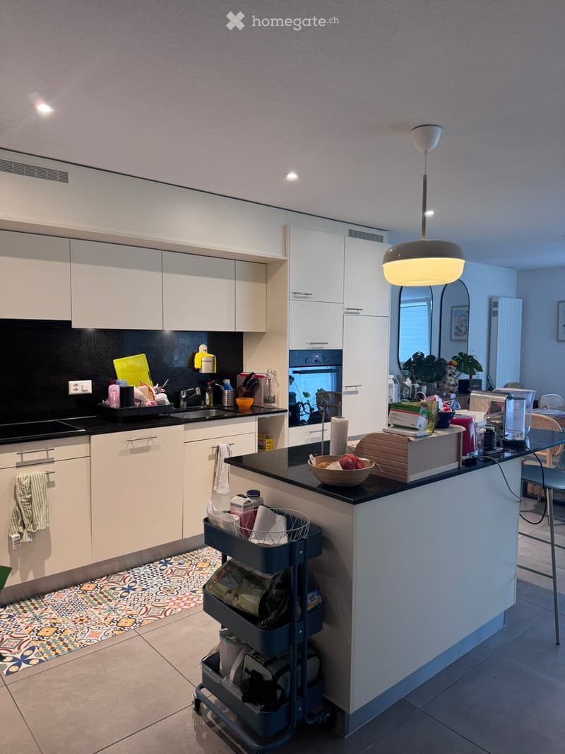 Modern kitchen with white cabinets, black countertop, sink, and various appliances. Features a central island with a bowl and a cart with storage compartments.
