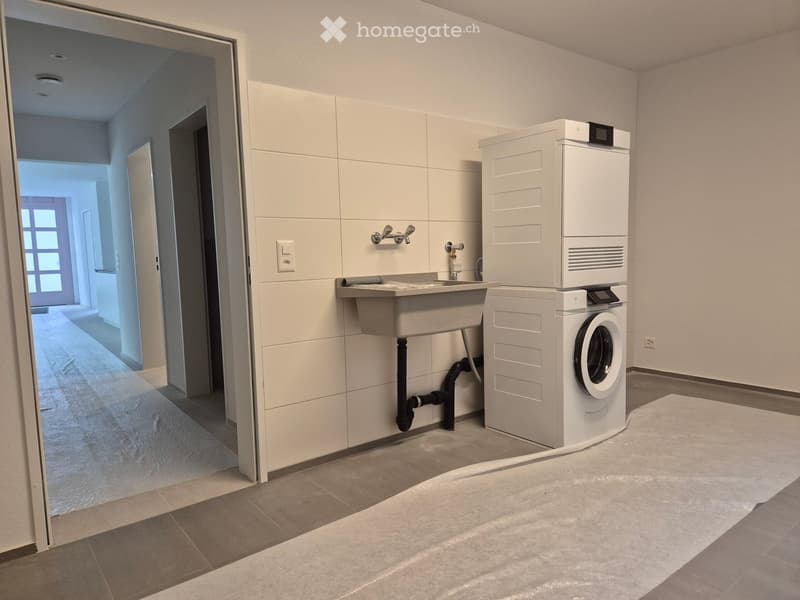 Modern bathroom with a sink, faucet, and stacked washing machine and dryer unit. The space features tiled walls and a tiled floor.
