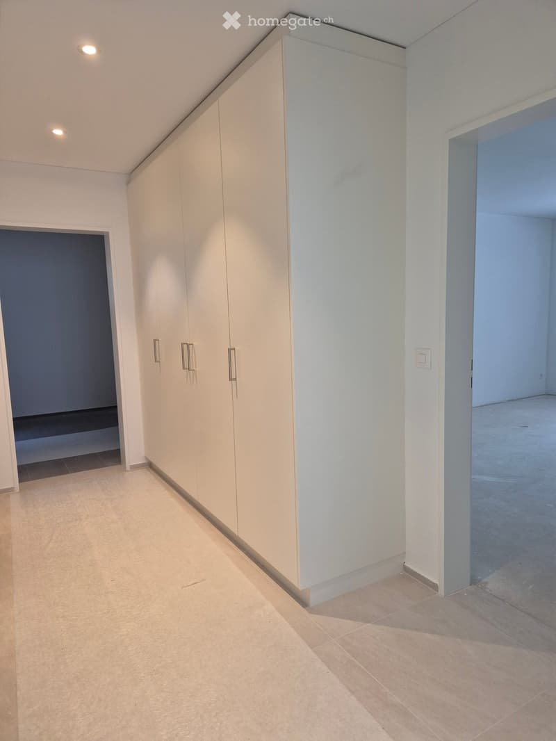Empty hallway with light-colored tiled flooring, white walls, built-in closet with silver handles, and recessed lighting.