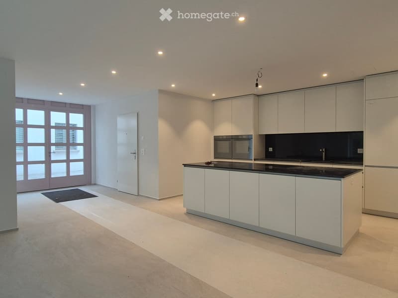 Modern kitchen with white cabinets, black countertop, and built-in oven. Features recessed lighting and large windows.