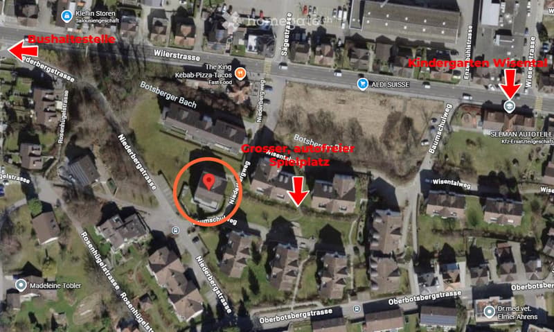 Aerial view of a residential area showing a highlighted building, surrounded by streets and nearby landmarks such as a kindergarten, a bus stop, and a large playground.