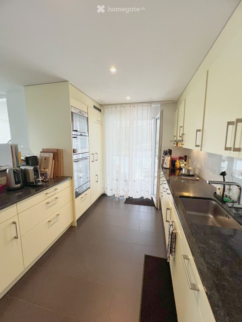 Modern kitchen with white cabinets, dark countertops, and stainless steel appliances. Features an oven, sink, and various kitchen items on the counters.