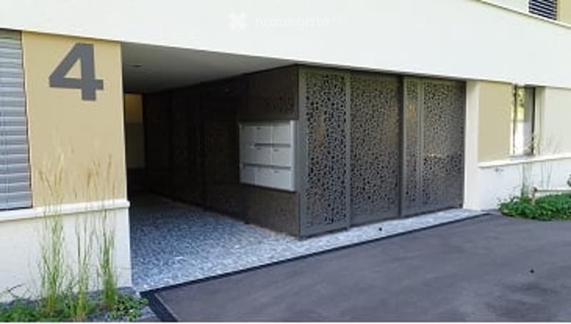Building entrance with a covered garage area, decorative metal gate, and a mailbox. The number "4" is displayed on the wall.
