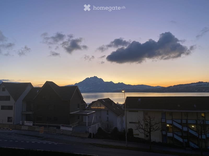 Residential buildings with modern architecture, situated near a body of water with mountains in the background during sunset.