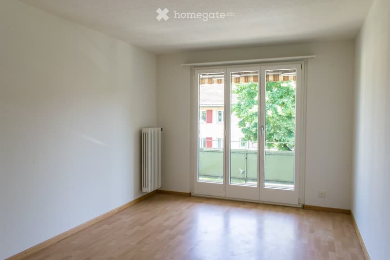 Empty room with wooden flooring, white walls, and a sliding glass door leading to a balcony or outdoor area.