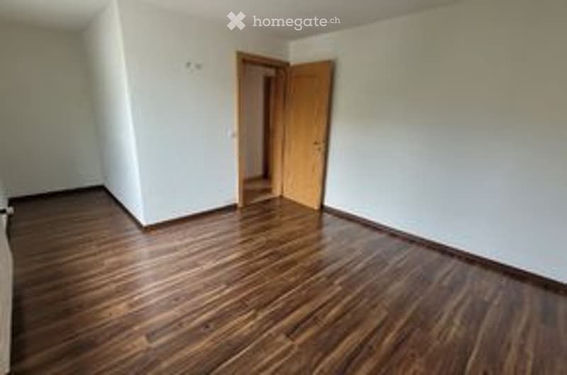 Empty room with wooden flooring and white walls, featuring a single open doorway leading to another space.