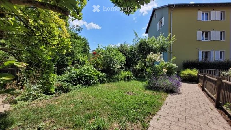 A well-maintained garden with a brick pathway leading to a wooden fence, surrounded by lush greenery and flowering plants.