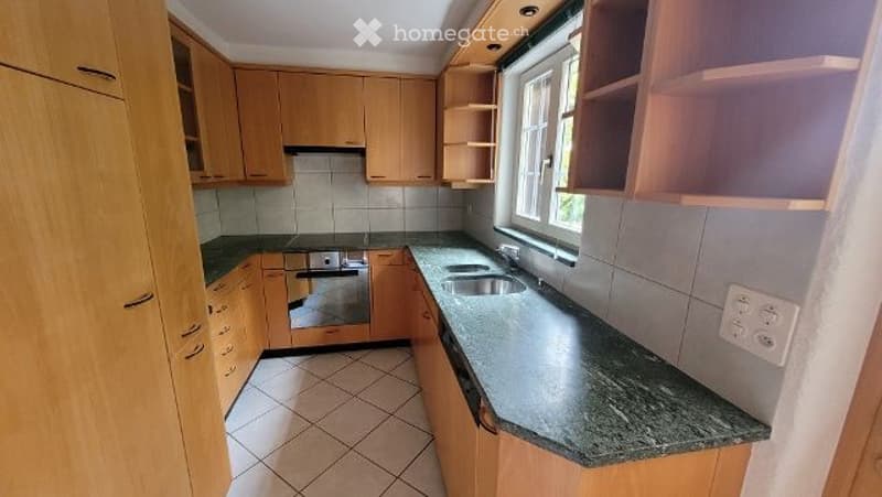 Modern kitchen with light wooden cabinets, granite countertop, stainless steel sink, and built-in oven.