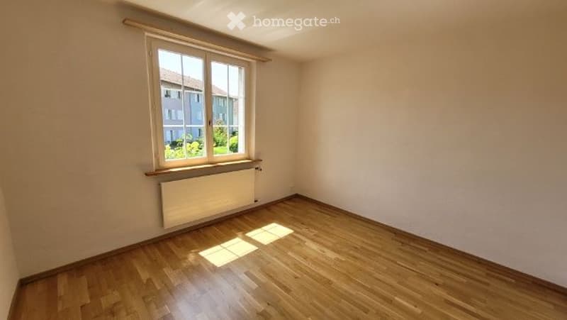 Empty room with wooden flooring, white walls, and a single window with a radiator below it. No furniture or equipment present.