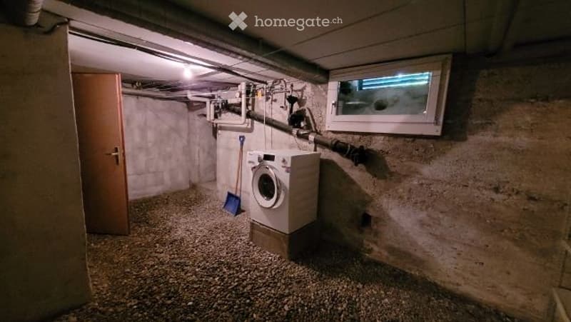 Underground laundry room with concrete walls, a washing machine, a broom, and a small window.