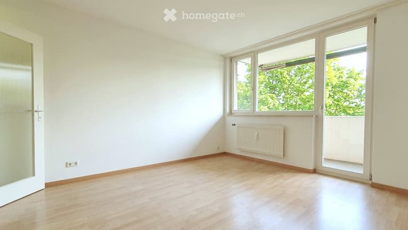 Empty room with light wooden flooring, white walls, large windows, and a radiator. No furniture or equipment present.