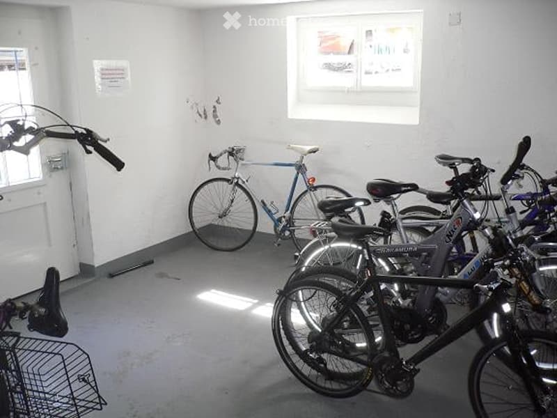 Empty room with several bicycles parked inside, white walls, and a window letting in natural light.