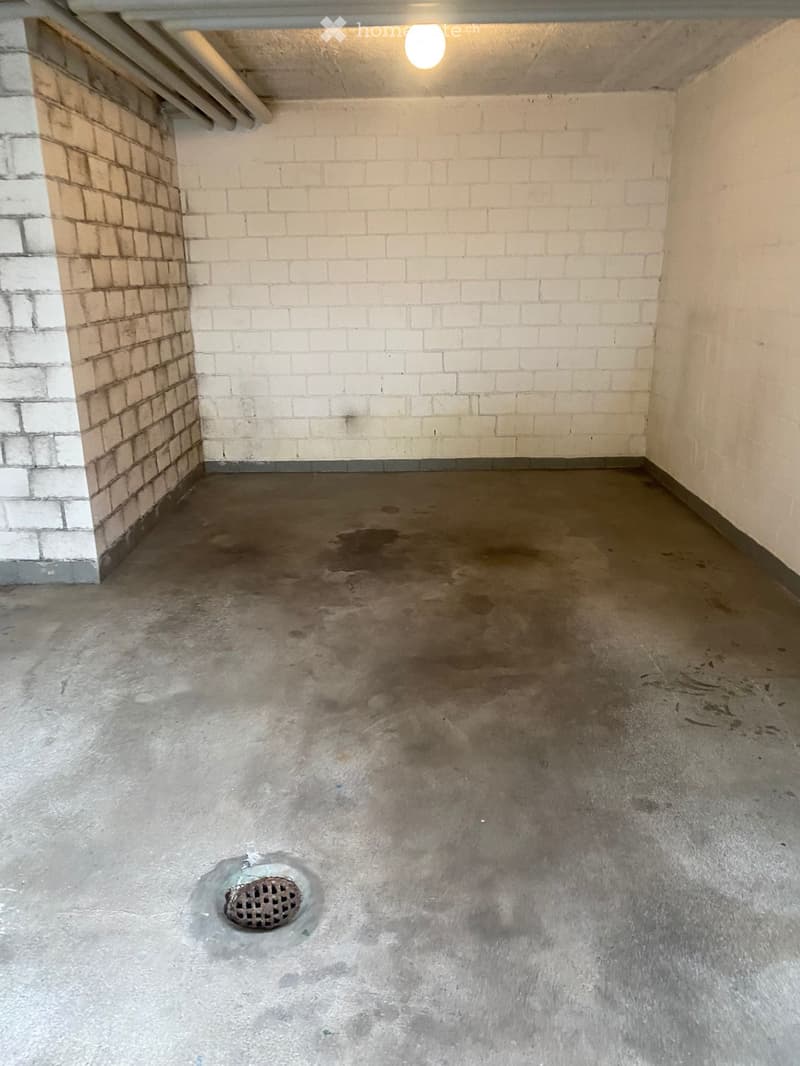 Empty concrete room with white brick walls, a single drain in the floor, and a small window on the left side.